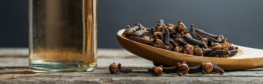 a bottle of clove oil next to a spoon of cloves