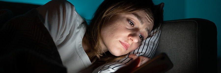 woman laying in bed looking at phone. blue light dangers.