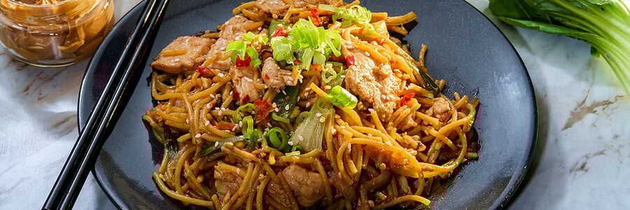 A bowl of stir-fried noodles with vegetables and chicken