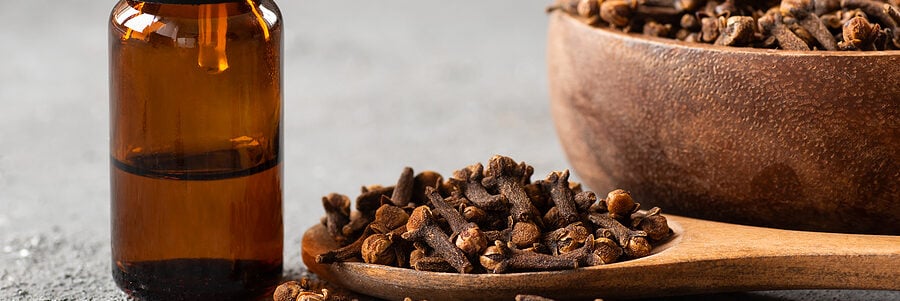 a bottle of clove oil next to a spoon of cloves