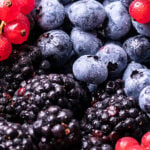 Close-up of a bowl filled with fresh blueberries, blackberries, and bright red currants, with water droplets visible on the berries.